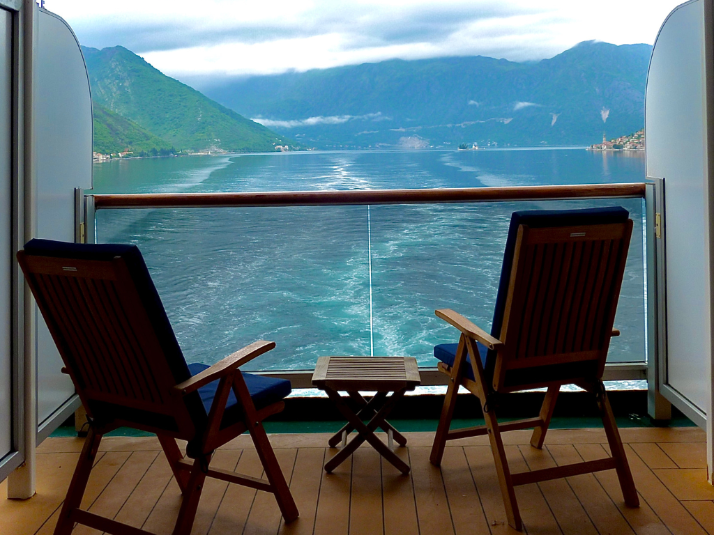 Woman on a cruise ship balcony overlooking a serene sea filled with anchored sailboats, enjoying the tranquil view