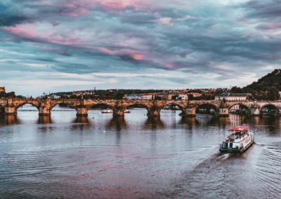 A picturesque river cruise passing under the historic Charles Bridge in Prague during a vibrant sunset.