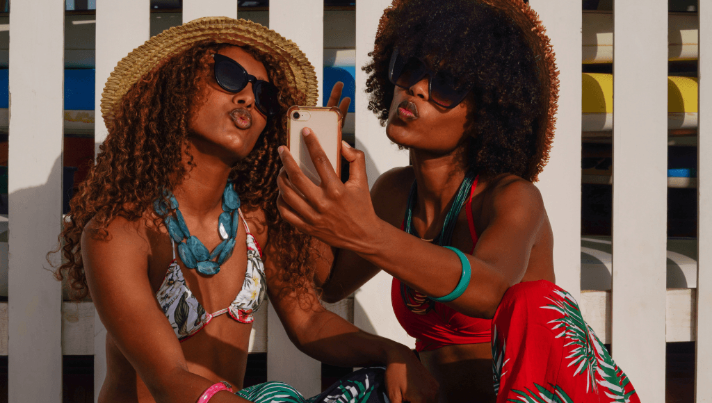 Two stylish women taking a selfie in summer outfits and hats, celebrating friendship and fun on Jamaican vacation.