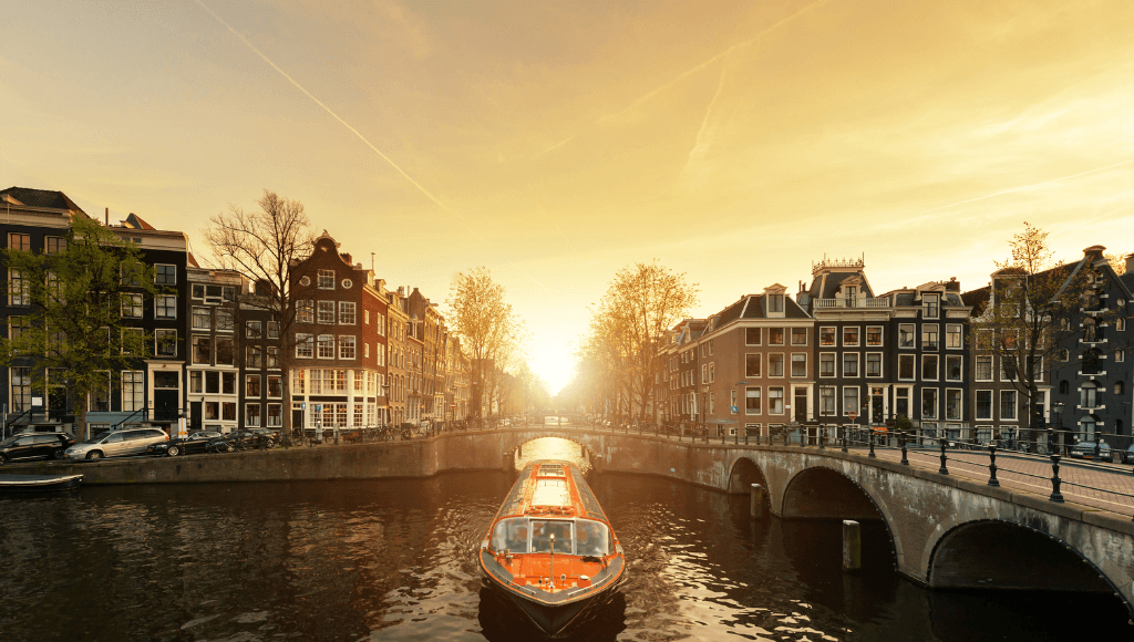 A picturesque canal cruise in Amsterdam at sunset, showcasing historic Dutch buildings and an illuminated boat.