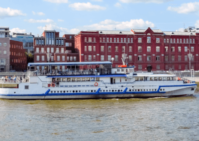 A modern riverboat on the Moskva River, passing by historic red-brick buildings in Moscow, Russia.