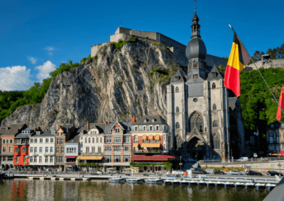 A scenic riverfront view in Dinant, Belgium, with colorful townhouses and the iconic Collegiate Church of Notre Dame.