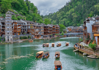 A tranquil river cruise in Fenghuang Ancient Town, China, with traditional Chinese architecture and small boats on the water.