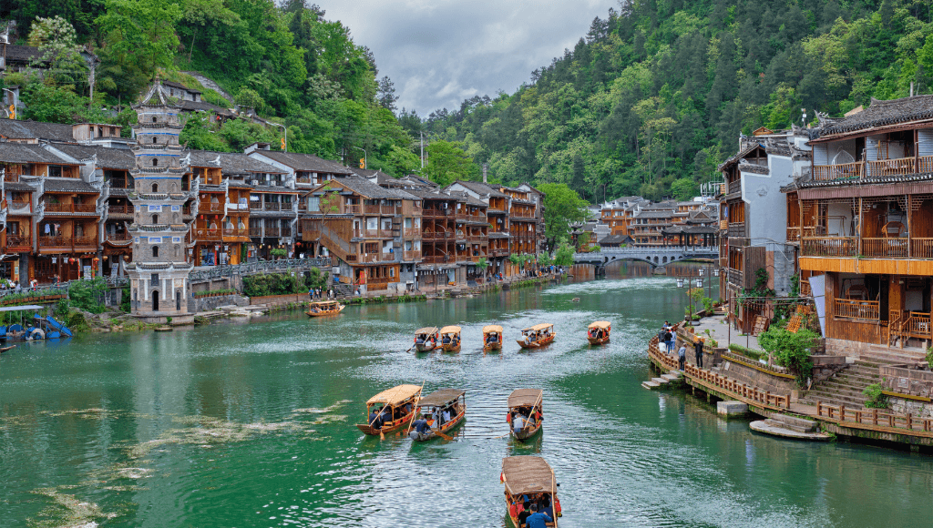 A tranquil river cruise in Fenghuang Ancient Town, China, with traditional Chinese architecture and small boats on the water.