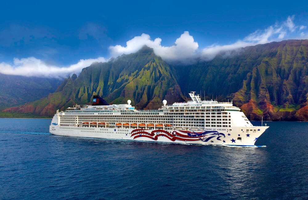 Norwegian Cruise Line's Pride of America sailing near the dramatic, cloud-covered cliffs of Hawaii's coastline.