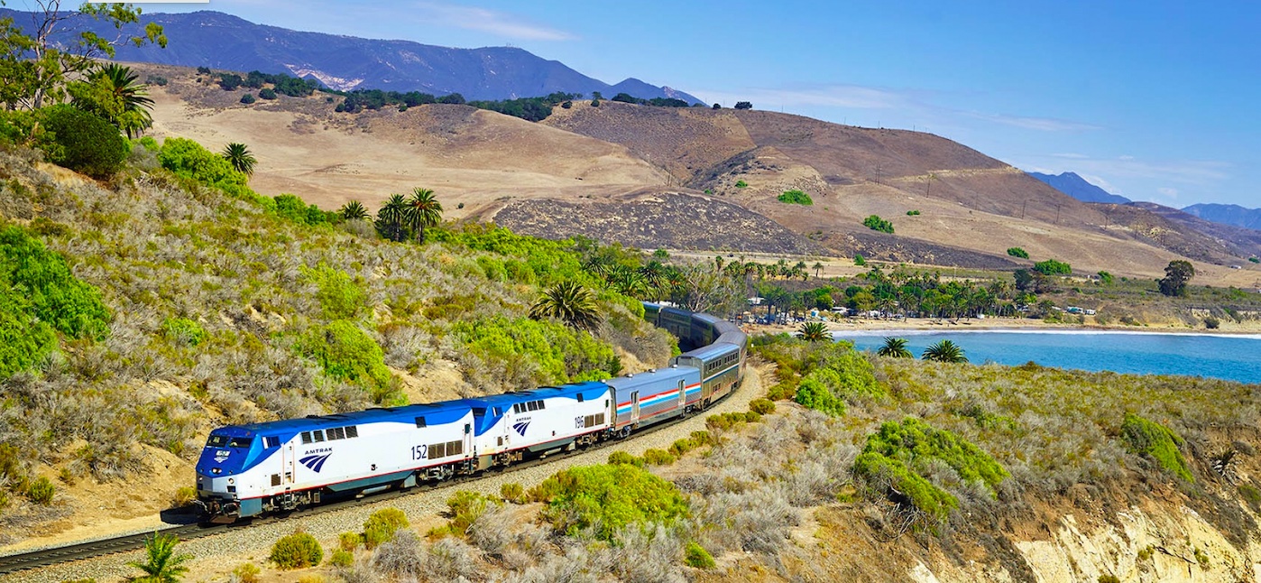 An Amtrak train traveling through a scenic, arid landscape with rolling hills and open skies.