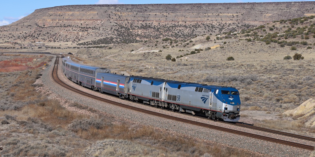 An Amtrak train traveling through a scenic, arid landscape with rolling hills and open skies.